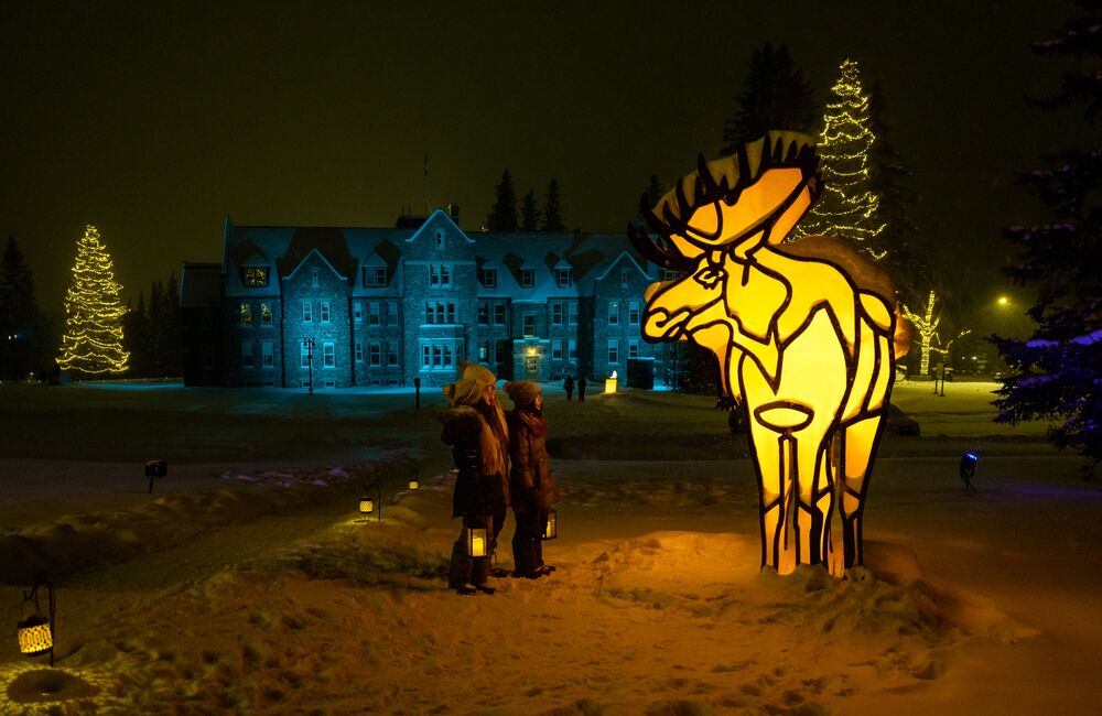 A family of three stand holding lanterns in front of a winter display with a moose in Banff National Park